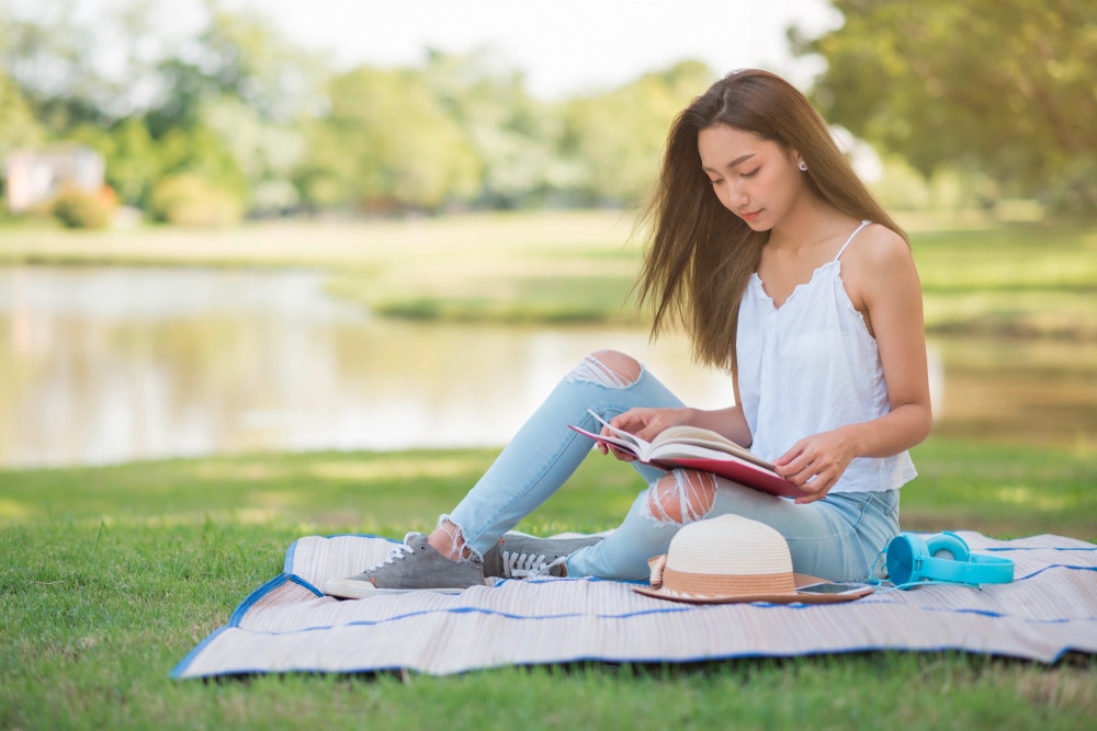 Woman with long hair reading book at the park.