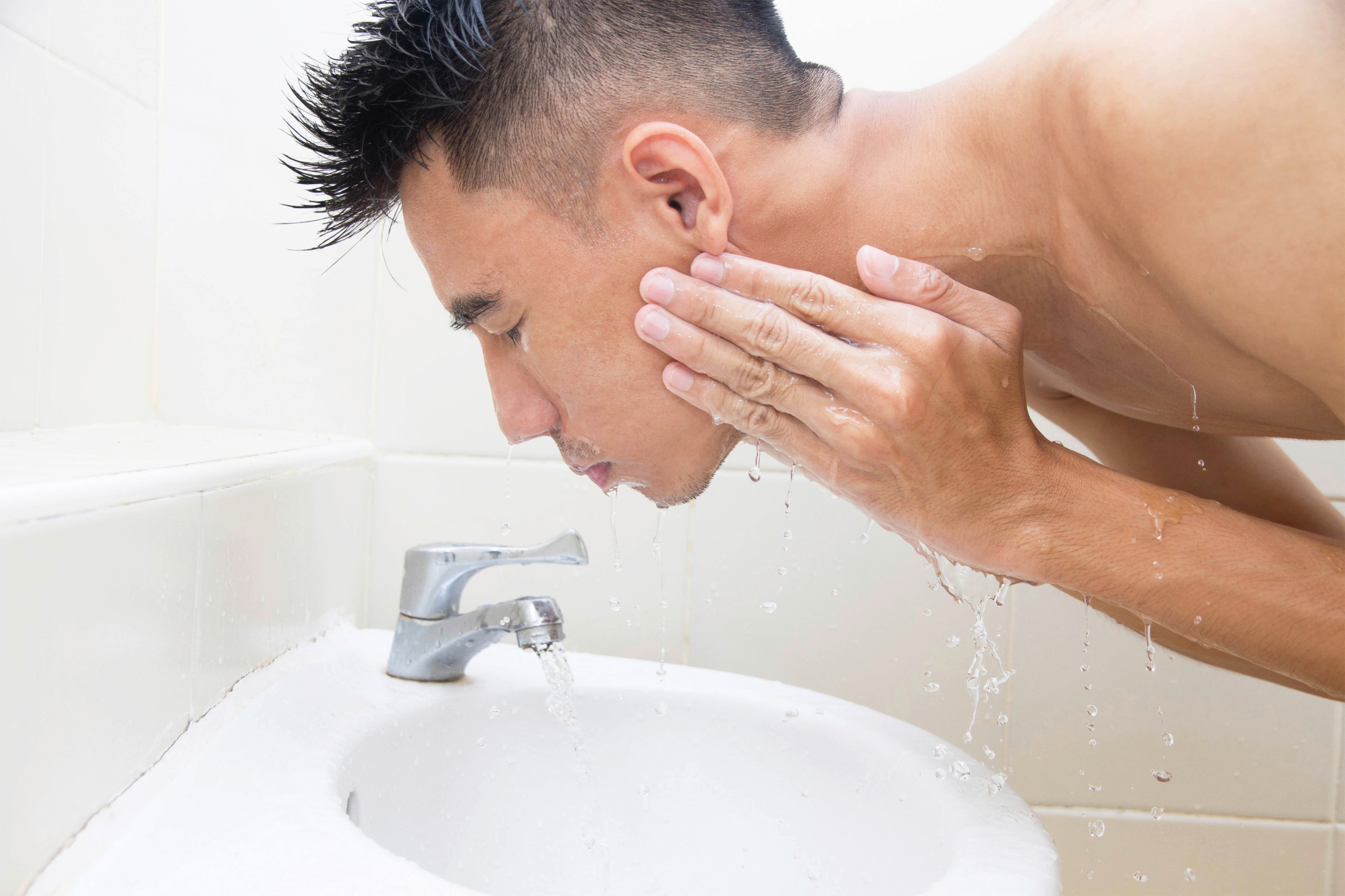 An Asian man washing face on the sink