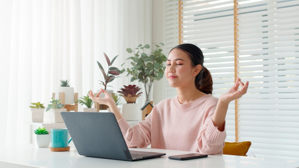 A woman meditating in front of her laptop.
