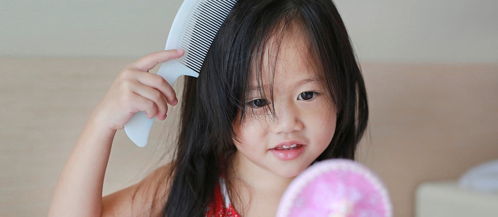 Seorang anak perempuan sedang menyisir rambutnya sambil melihat ke cermin kecil