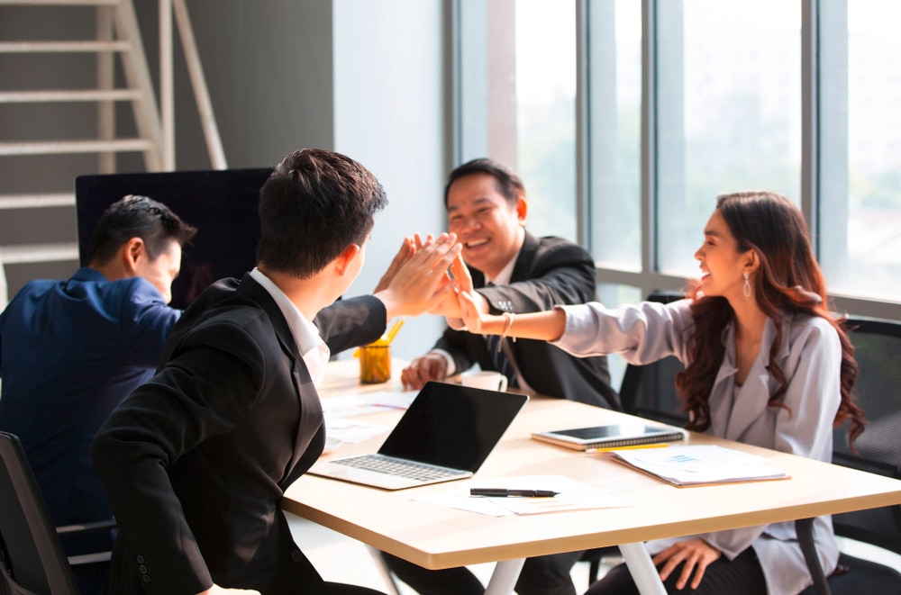 Four people wearing business suits doing a high-five at work.