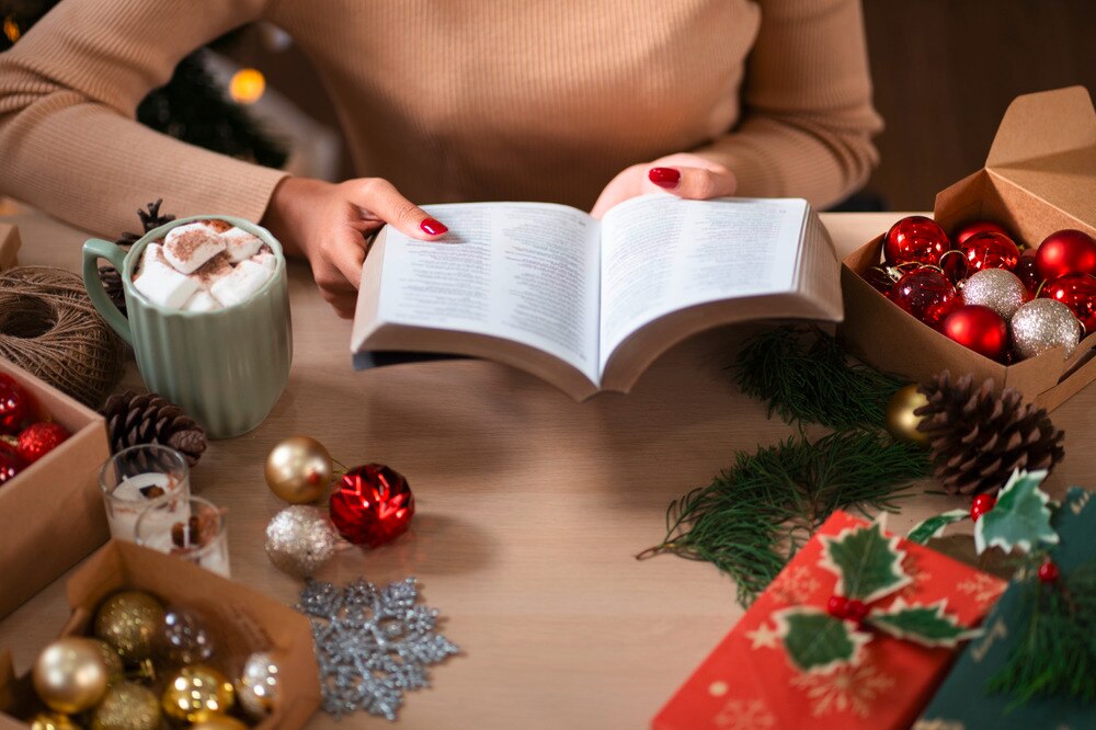 Closeup of a woman’s hands holding a book surrounded by Christmas décor.