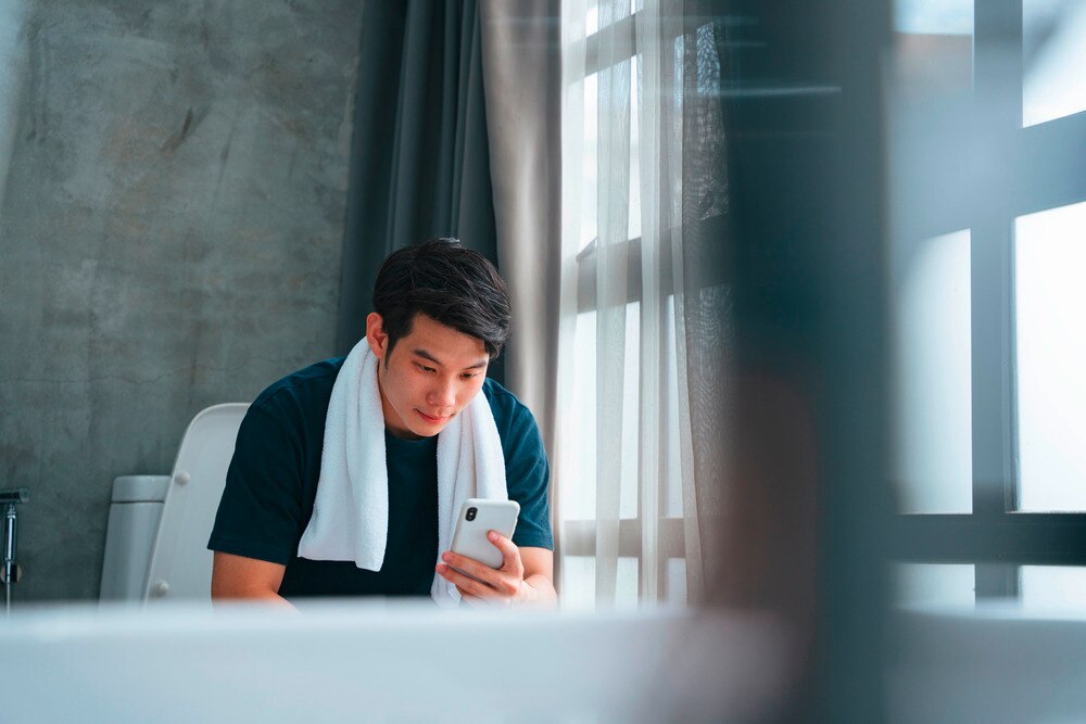 Man looking at his phone while sitting on a toilet.