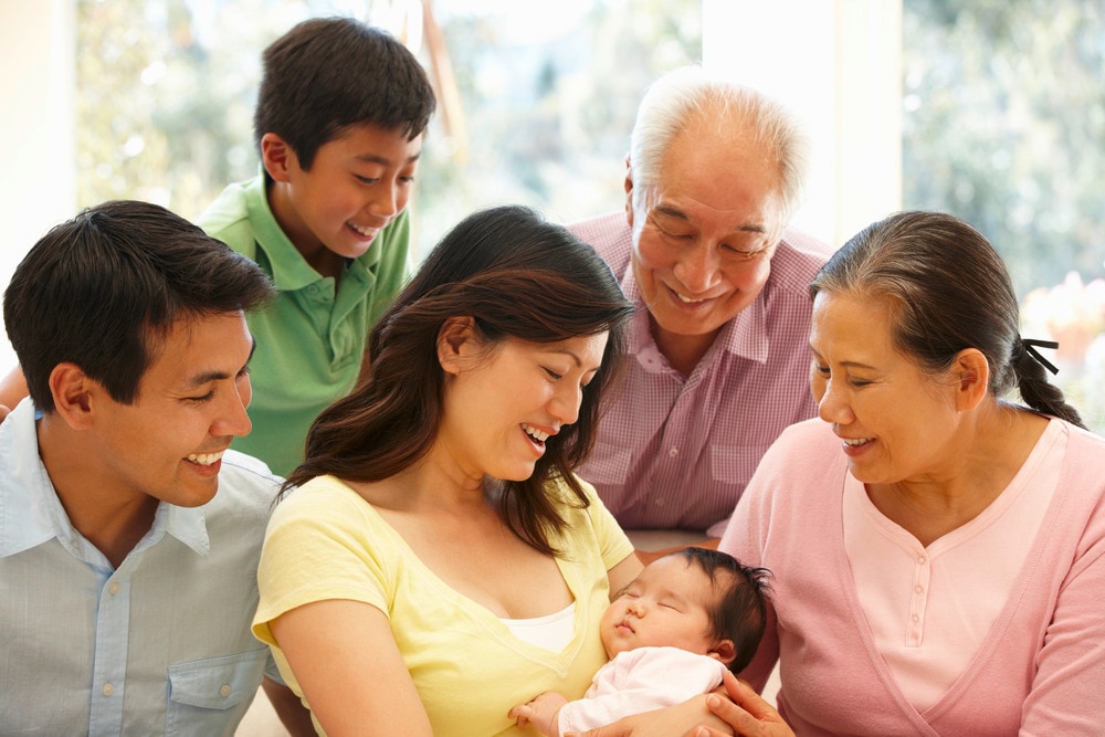 Asian family with mom, dad, brother, and grandparents looking at a newborn.