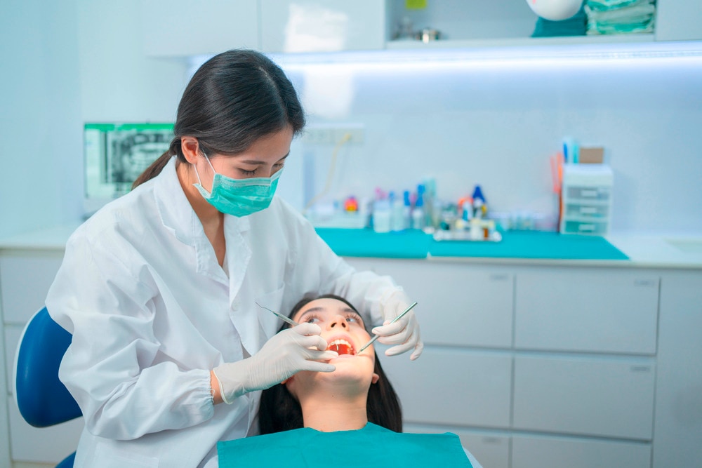 Female dentist cleaning her patient’s teeth with a scaler.