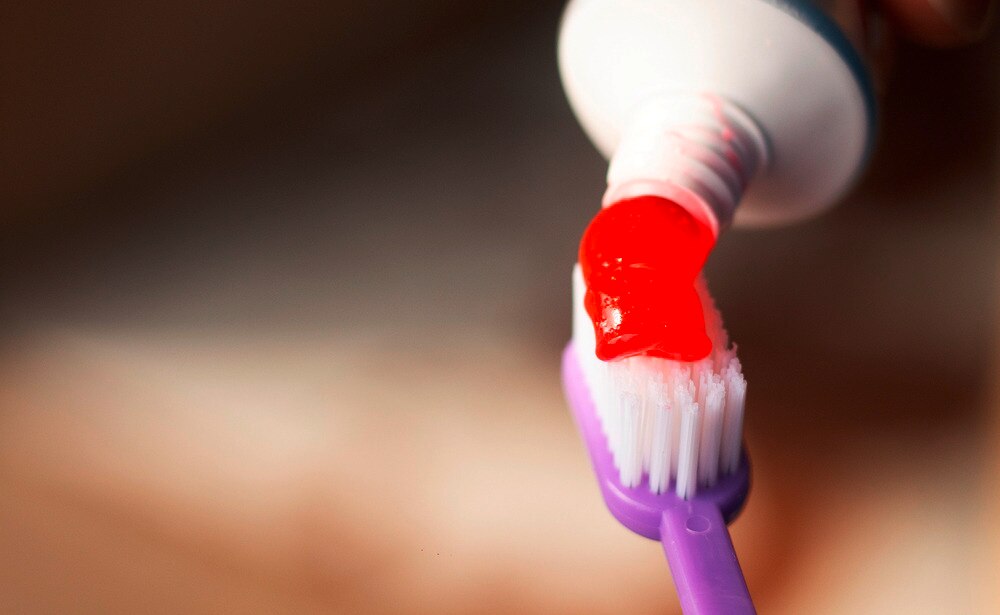 A person squeezing toothpaste out of the tube and onto a toothbrush. 
