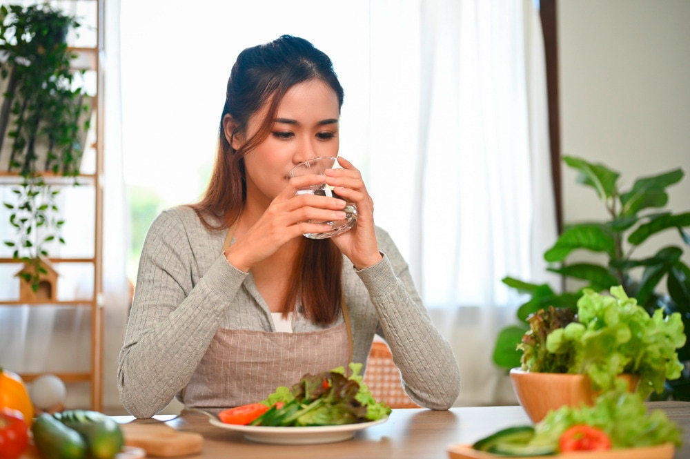 Woman drinking a glass of water with a plate of salad on her table.