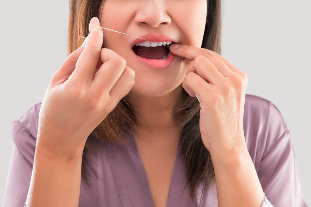Woman in a bathrobe flossing her teeth.