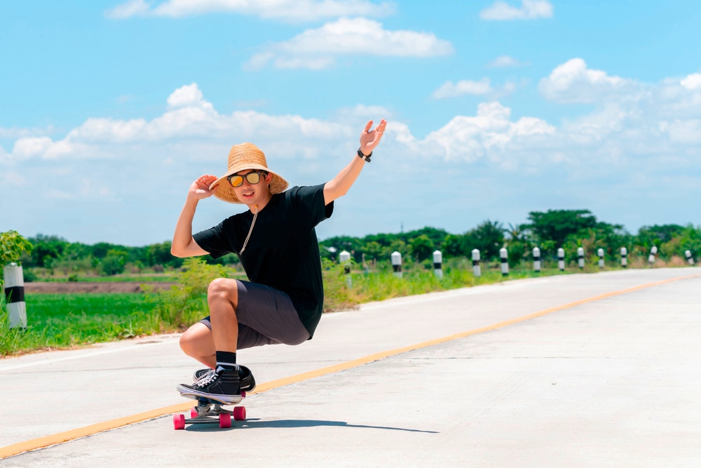 Man in black shirt and straw hat riding skateboard.