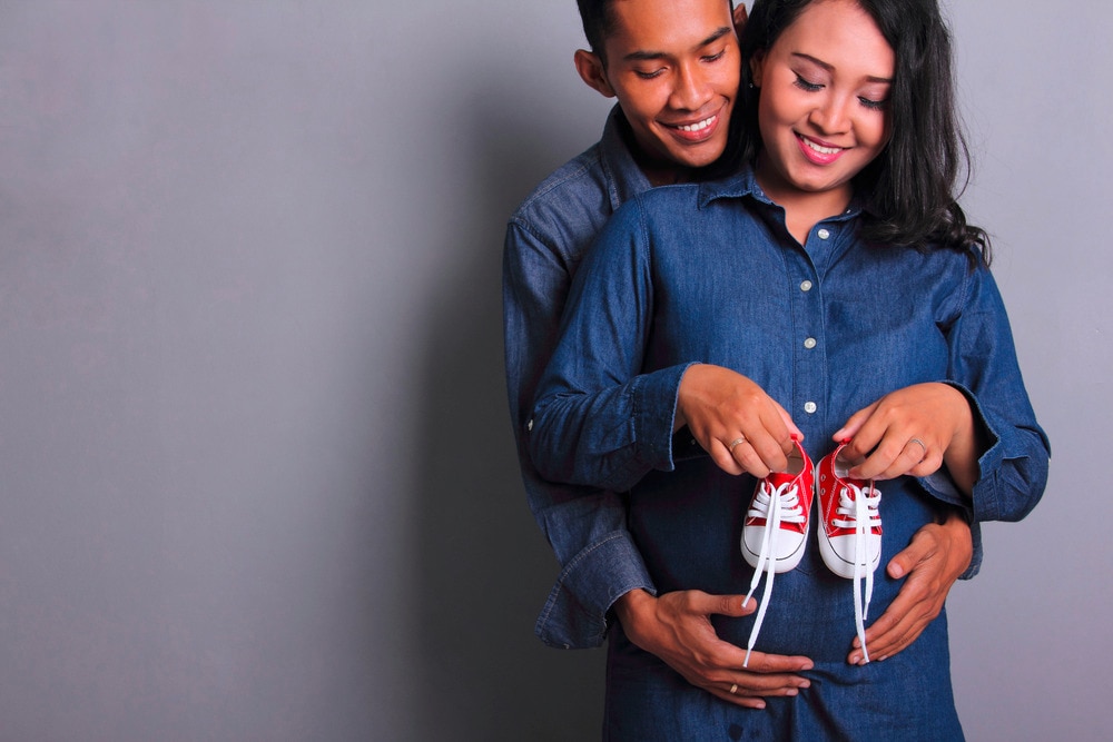 Happy parents-to-be posing with a pair of baby shoes.