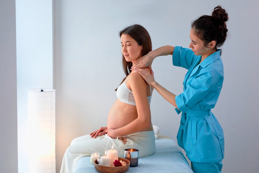 Pregnant woman massaged by a female therapist on her neck and shoulders.