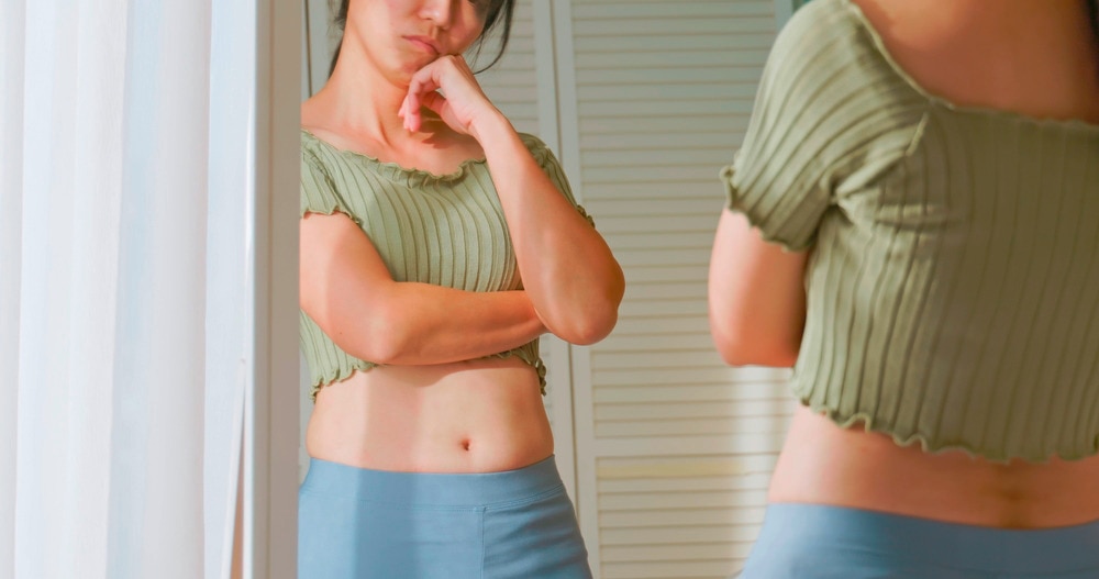 Asian woman in a green crop top looking at herself in a mirror.