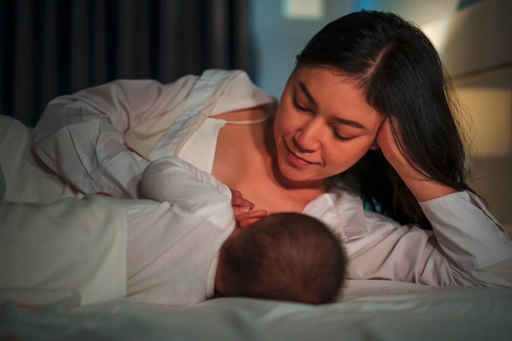 Mother breastfeeding her baby while lying on a bed.
