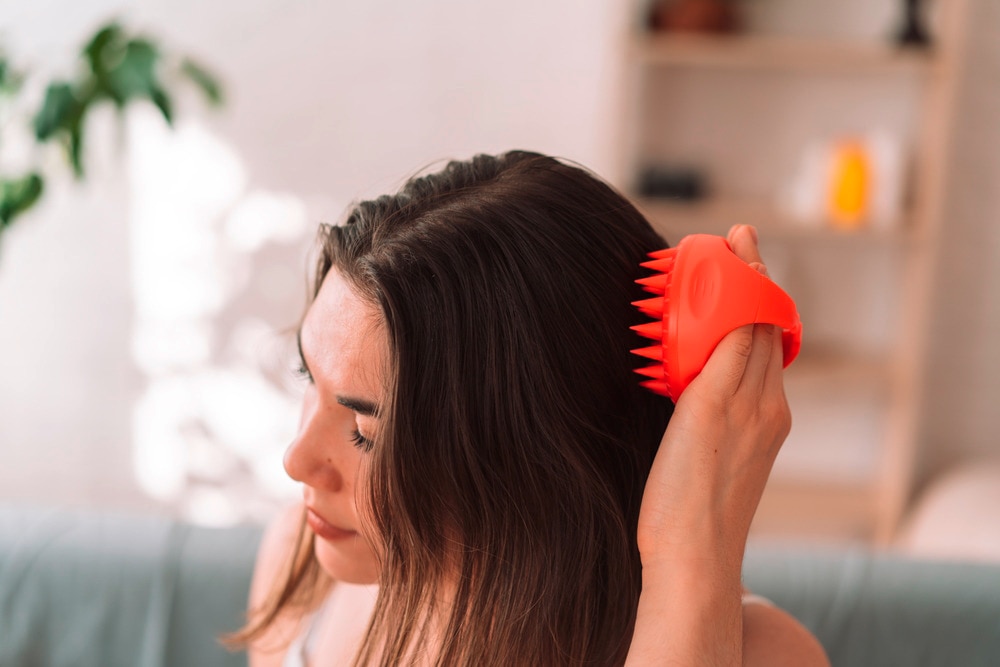 Woman massaging her hair with a silicone brush.