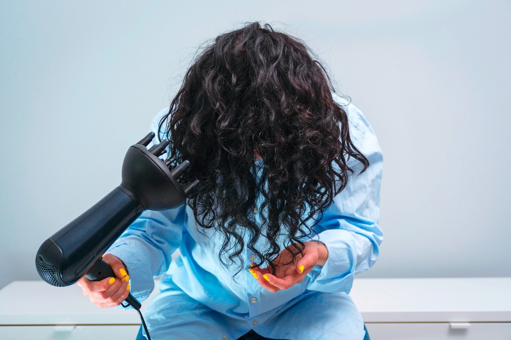 Woman with her curly hair upside down holding a hairdryer with a diffuser nozzle.