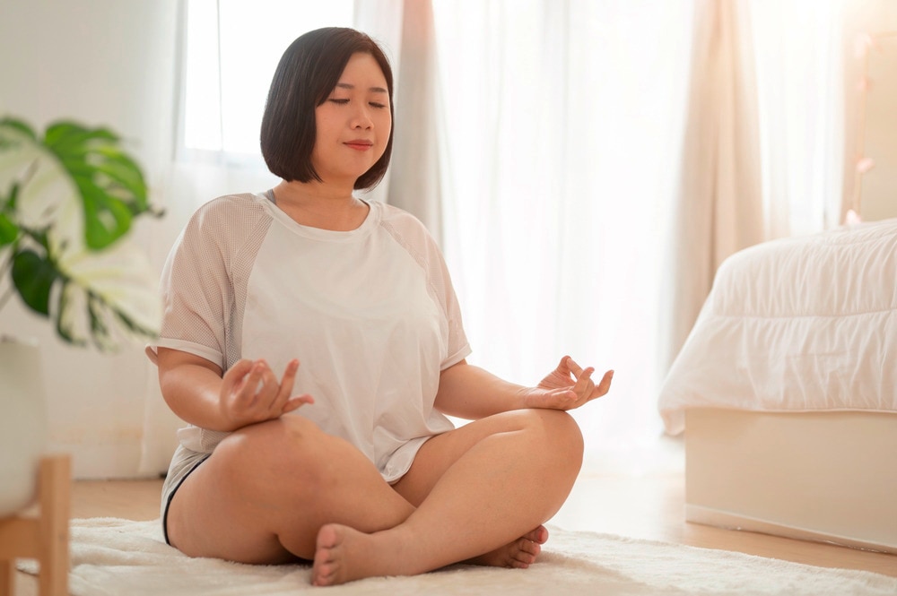 Plus-size woman meditating in her bedroom.