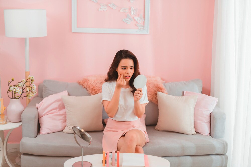 Woman checking her face in the mirror with a worried look.
