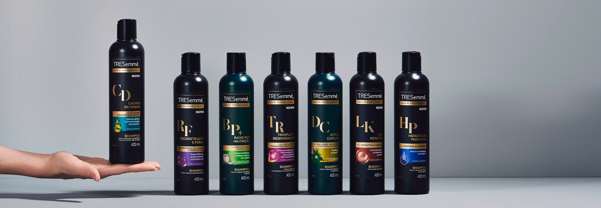 Sete embalagens variadas de shampoo, inclusive uma que está em cima de uma mão estendida à esquerda