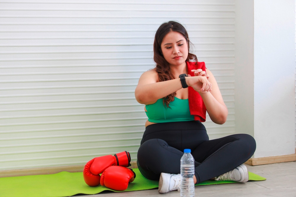  Asian woman in green and black looking at watch with boxing gloves.