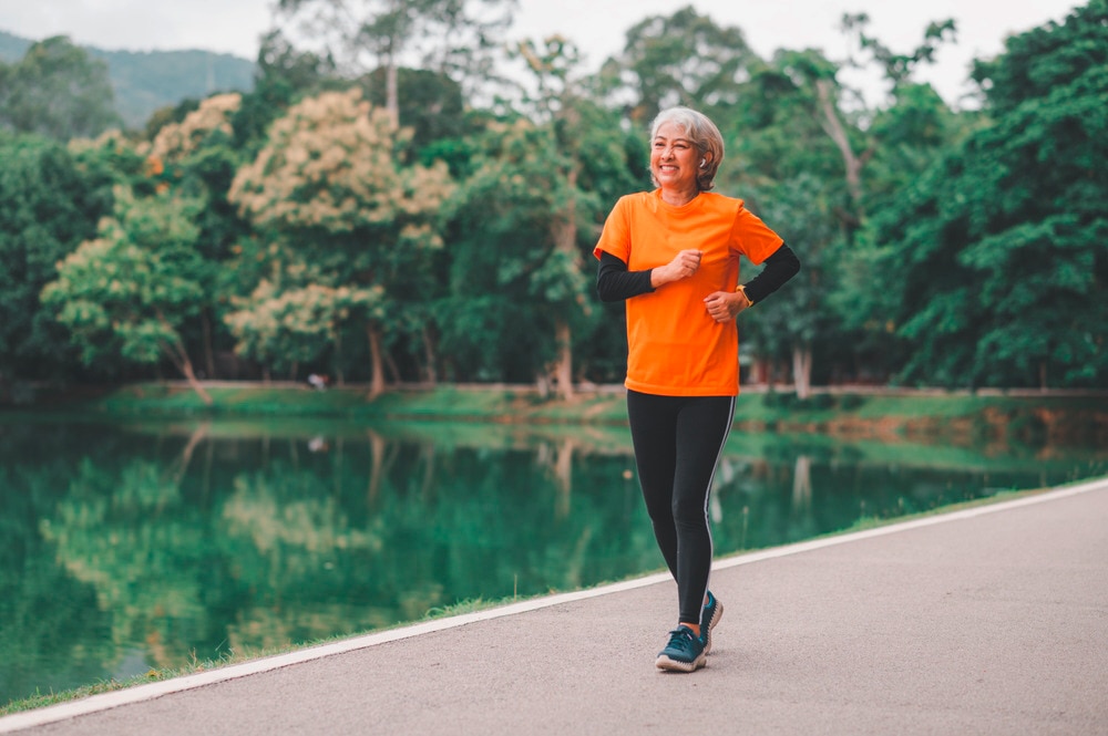 Middle-aged Asian woman running around a lake in orange and black.