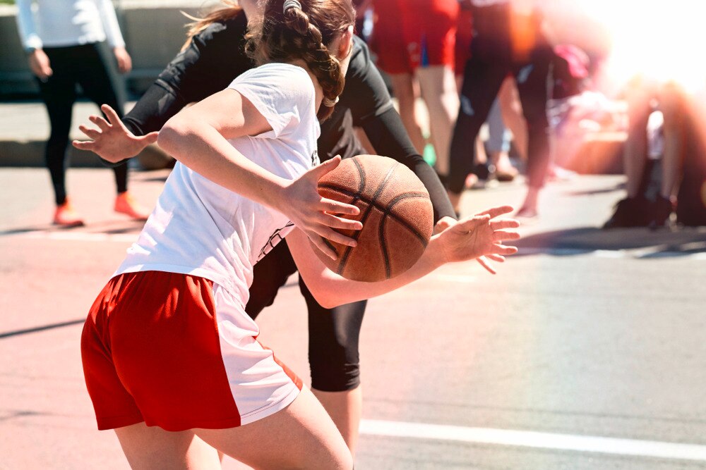 Woman in white top and gym shorts playing basketball against an opponent.