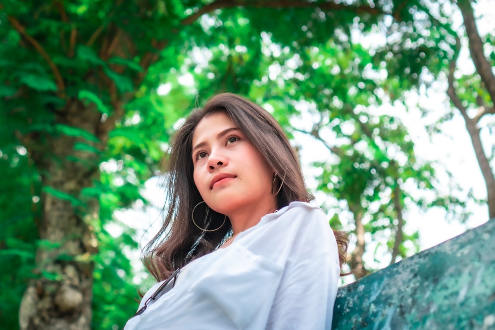 Woman with long hair sitting on a bench outdoor.