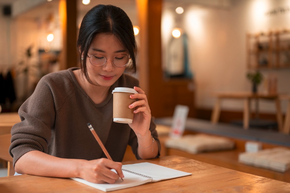 Woman writing in a notebook while drinking coffee.