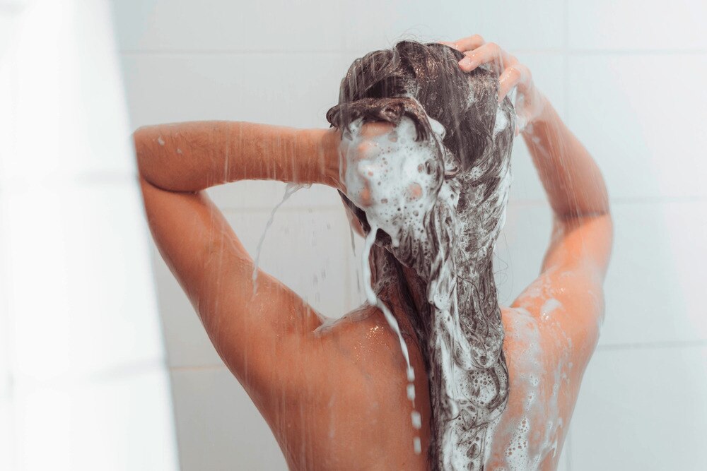 Woman washing her hair with shampoo in the shower.