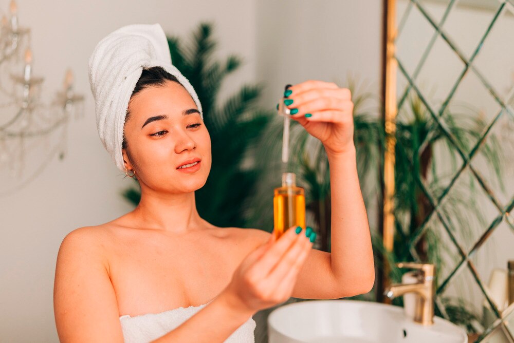 Woman in towel applying face serum.