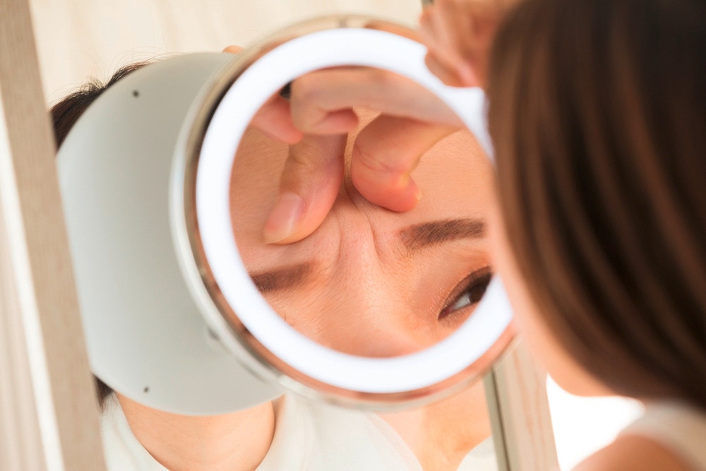 Woman looking at her wrinkles up close in a mirror.