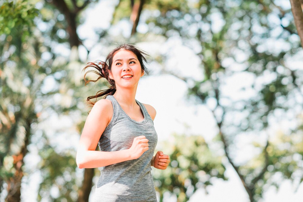 Woman in gray sleeveless top jogging around the park.