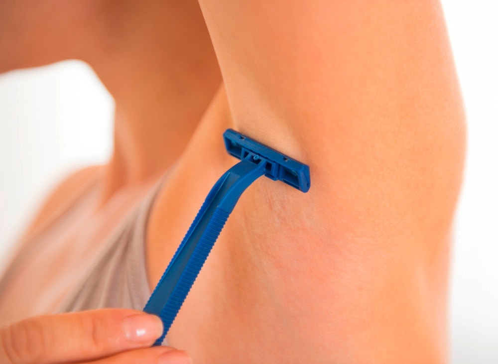 Woman shaving her underarms with blue razor.
