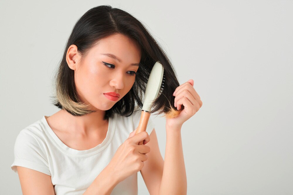 Woman brushing her short hair with a concerned expression.