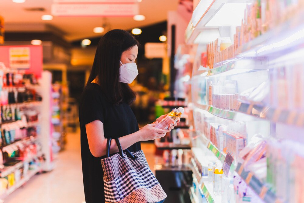 Woman in protective mask reading the ingredient list on a shampoo bottle.