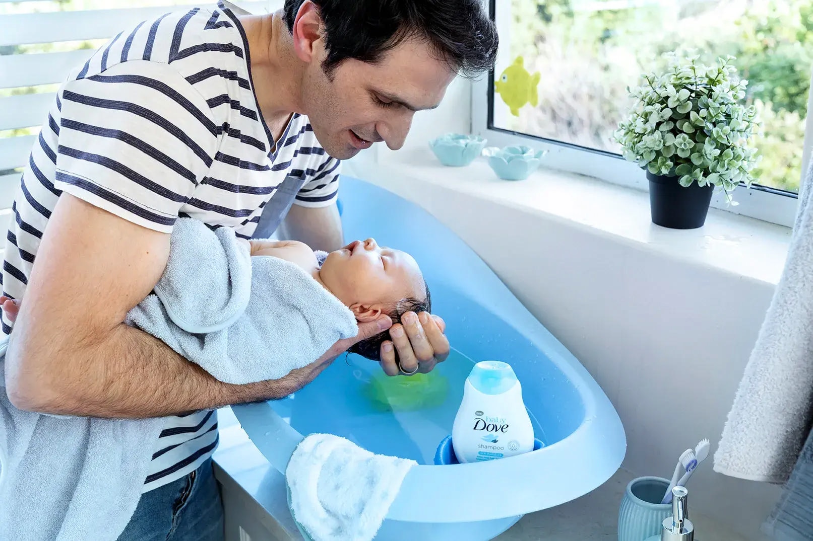 Dad leaning over bath whilst bathing newborn