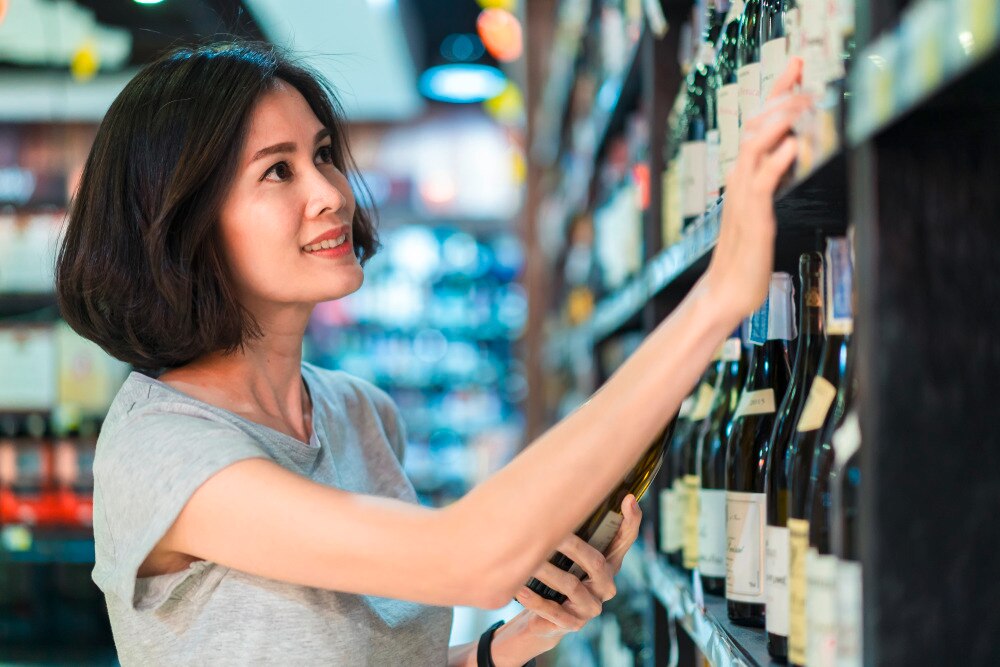 Asian woman looking at wine labels in the store.