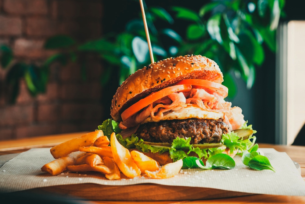A big hamburger with French fries on parchment paper.