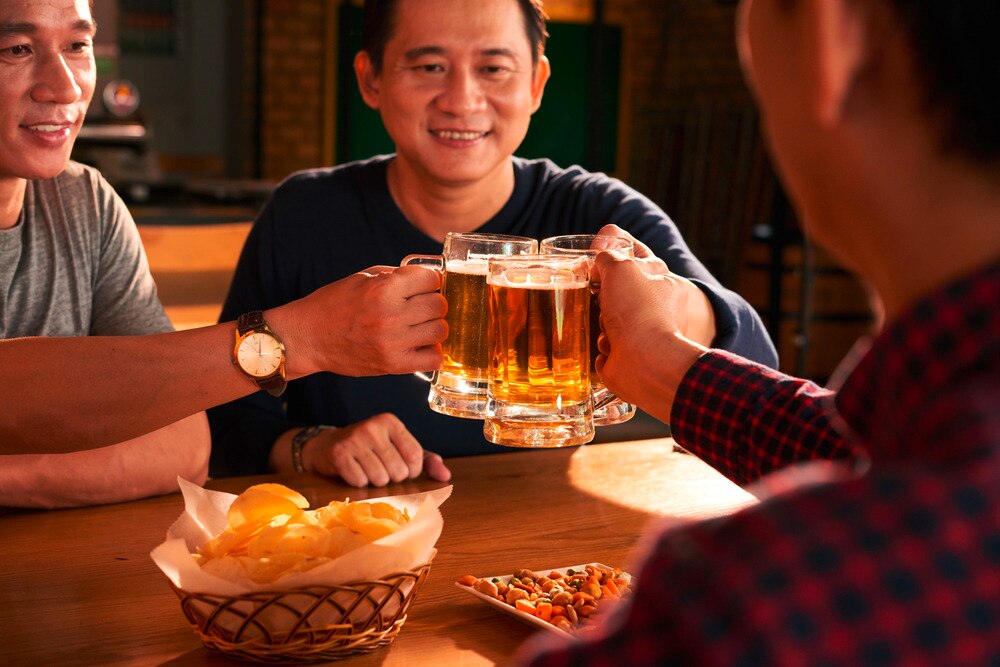 Asian men drinking beer in glass mugs in a bar.