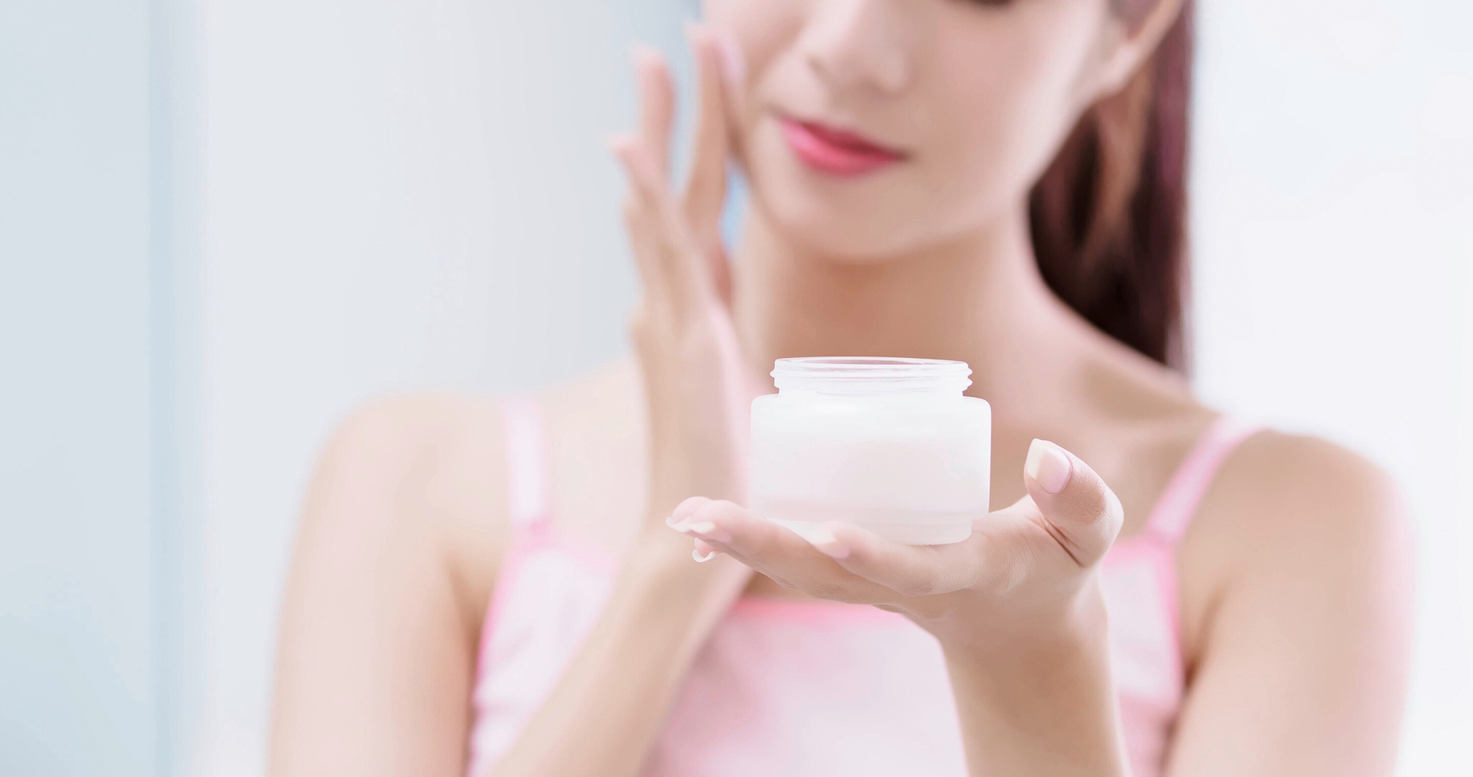 A woman holding a moisturizer product and applying it on her face 