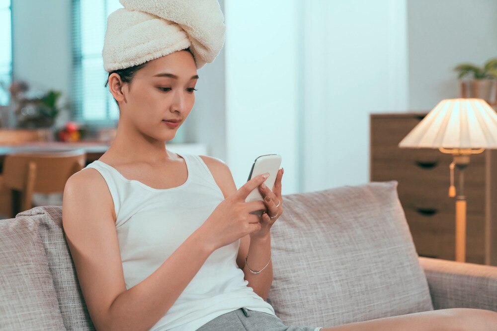 Woman with towel wrapped on her head playing with her phone.