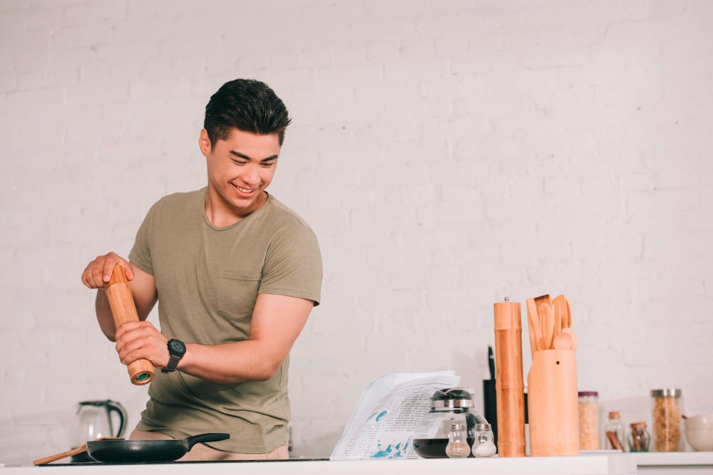Smiling man cooking in the kitchen while reading a newspaper.