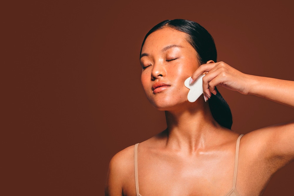 Woman massaging her face with gua sha tool.