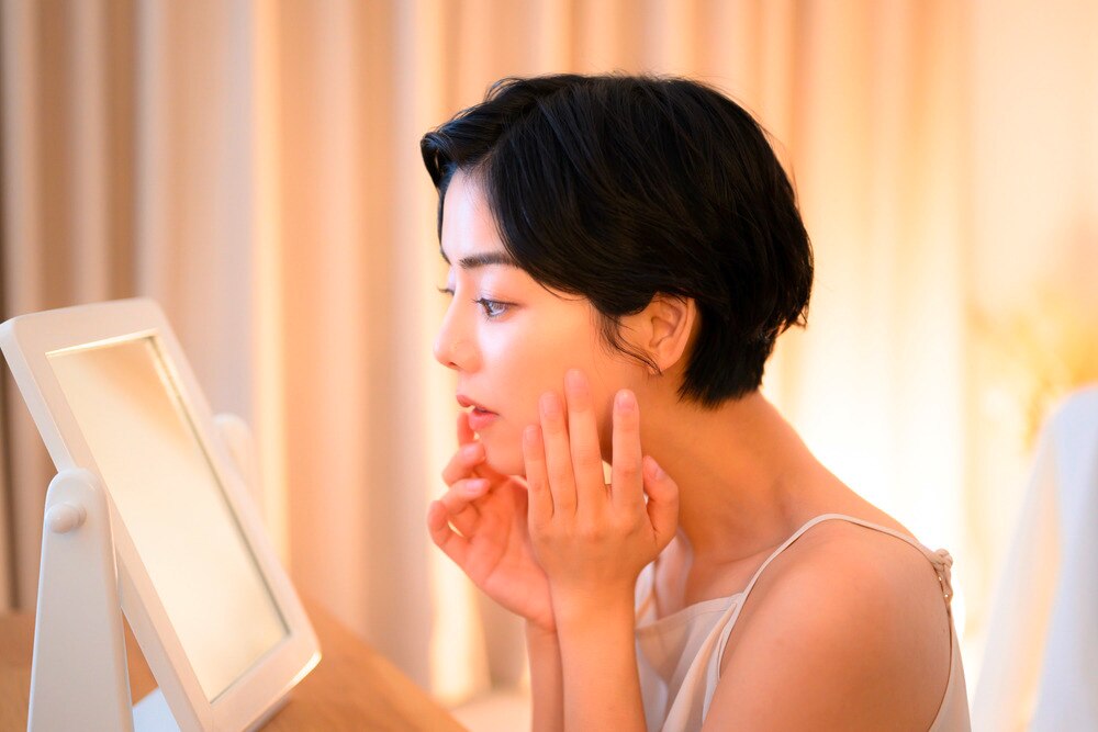 Woman applying serum to her face while looking in a mirror.