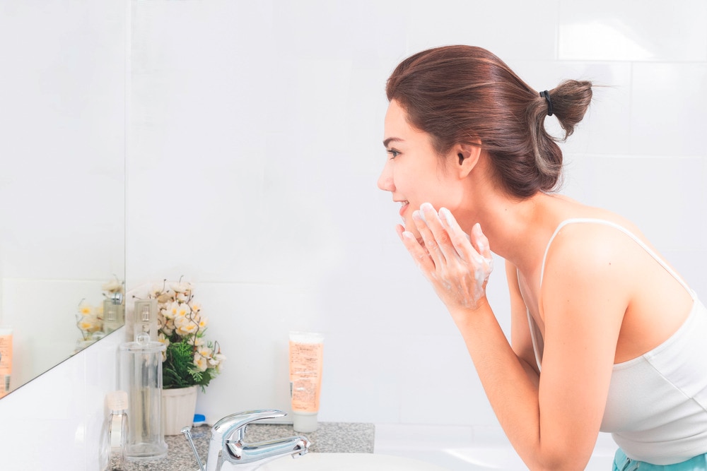 Woman using a cleansing balm to remove makeup on her face.