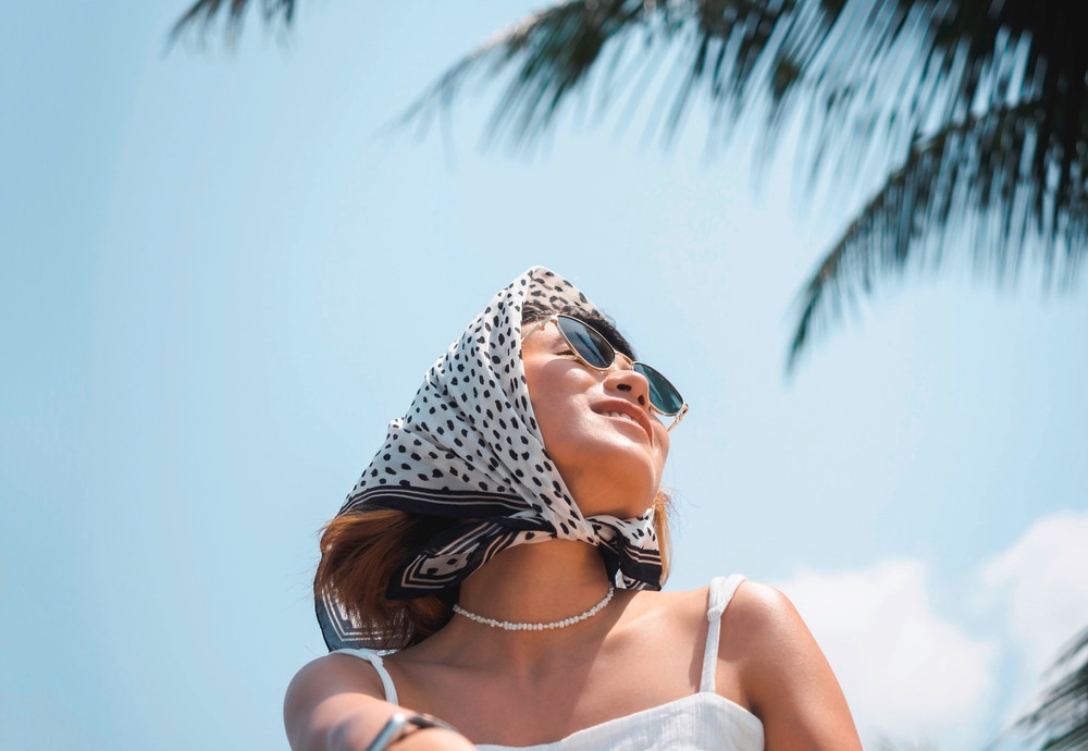 Asian woman in sunglasses and a bandana outdoors.