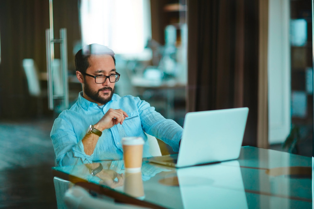 Man with glasses working with laptop on the table.