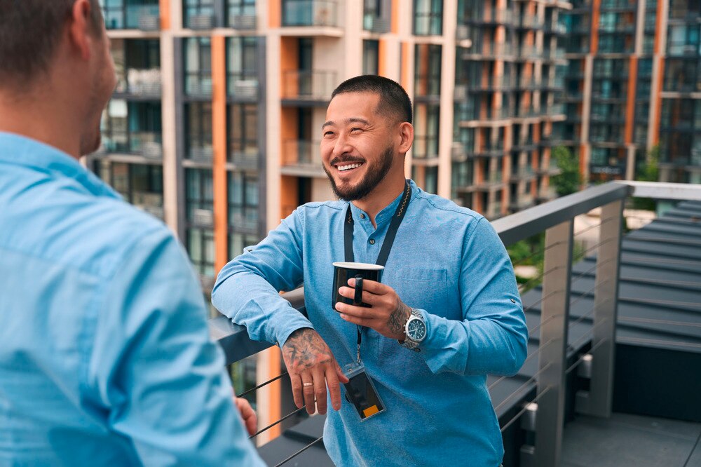 Smiling man talking with a male colleague while holding a cup.