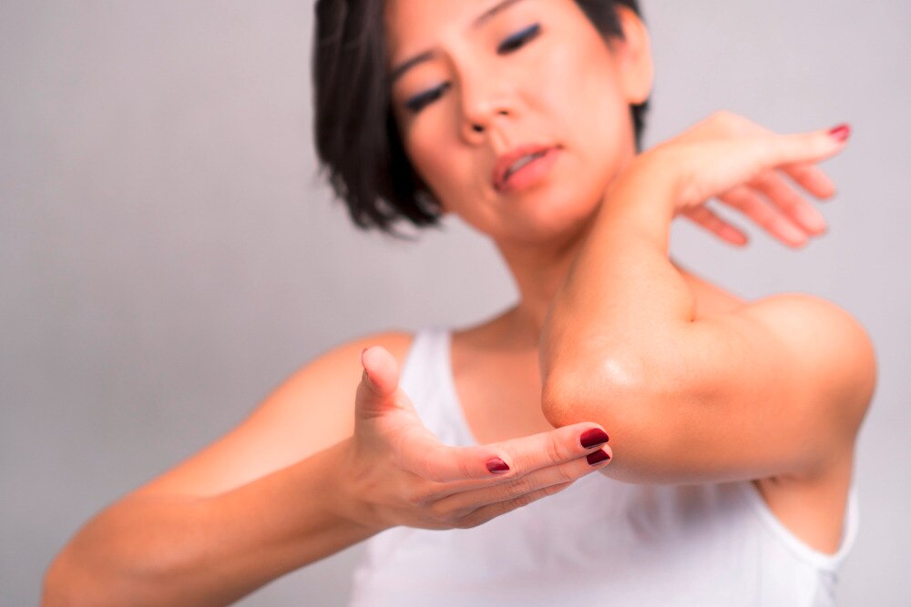 Asian woman touching her elbow.