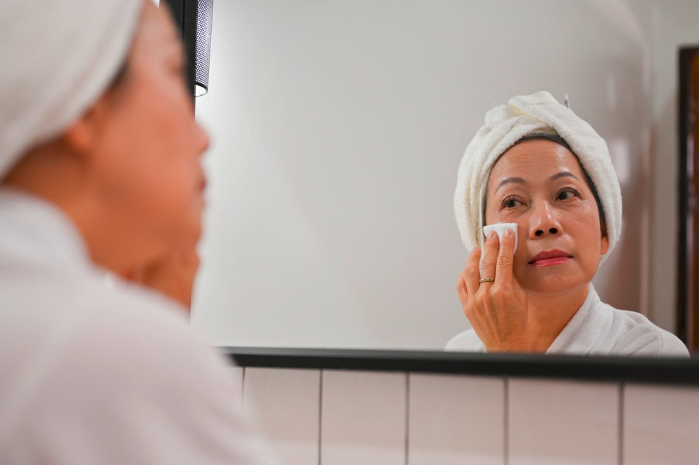 Older woman cleaning her face with cotton pad.