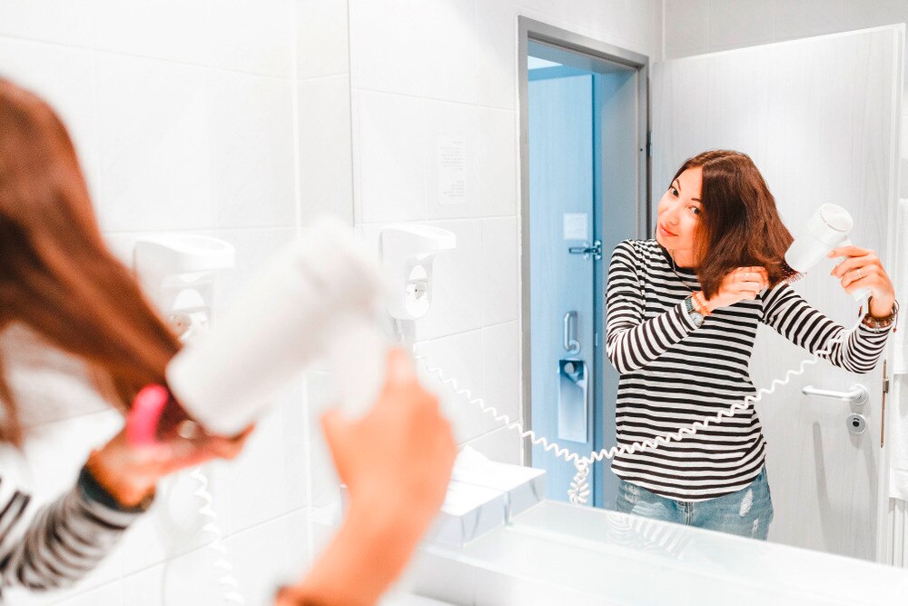 Woman blow-drying her short hair with a round brush.